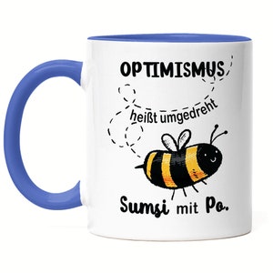 Può includere: Tazza in ceramica bianca con bordo e manico blu. La tazza presenta un'ape di cartone animato nera e gialla con il testo "Optimismus heisst umgedreht Sumsi mit Po."