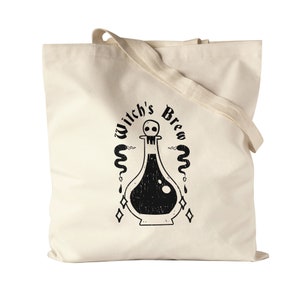 Op de afbeelding: Een witte canvas tote bag met zwarte tekst en een afbeelding van een drankfles met een schedel op de stop. De tekst luidt "Witch's Brew".