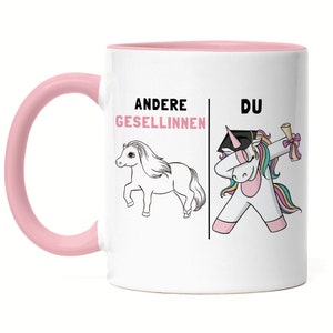 Könnte beinhalten: Weiße Keramiktasse mit rosafarbenem Rand und Henkel. Die Tasse zeigt auf der linken Seite eine Schwarzweißillustration eines Einhorns und auf der rechten Seite eine farbige Illustration eines Einhorns mit einem Abschluss-Hut. Der Text "Andere Gesellinnen" befindet sich über dem Schwarzweiß-Einhorn und der Text "DU" über dem bunten Einhorn.