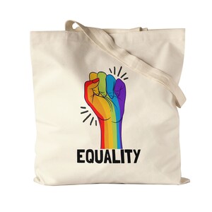 Op de afbeelding: Een witte canvas tote bag met een opgeheven regenboogvuist en het woord "GELLIJKAARDIGHEID" eronder.