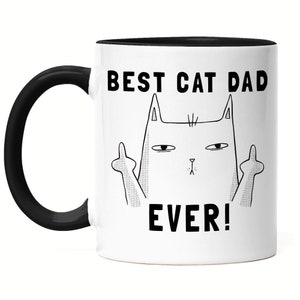 Może przedstawiać: Biały ceramiczny kubek do kawy z czarnym rantem i uchwytem. Kubek ma czarno-białą ilustrację kota pokazującego środkowy palec z tekstem "Best Cat Dad Ever!" nadrukowanym na nim.