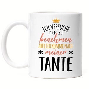 Könnte beinhalten: Weiße Keramiktasse mit einem schwarzen und goldenen Design. Die Tasse zeigt den Text "Ich versuche mich zu benehmen aber ich komme nach *meinen* TANTE".