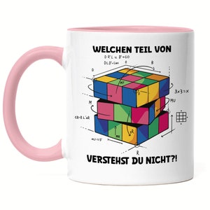 Puede incluir: Taza de cerámica blanca con asa rosa. La taza presenta una ilustración colorida de un cubo de Rubik con el texto "WELCHEN TEIL VON" y "VERSTEHST DU NICHT?!" en negro.