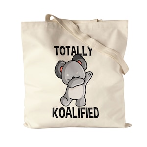 Könnte beinhalten: Eine beige Tragetasche mit einer schwarz-weißen Grafik eines Koalabären, der den Dab macht. Der Text "TOTALLY KOALIFIED" ist auf die Tasche gedruckt.