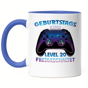 Könnte beinhalten: Weiße Keramiktasse mit blauem Rand und Henkel. Die Tasse zeigt eine Grafik eines lila und schwarzen Videospielcontrollers mit dem Text "Geburtstagskind Level 20 Freigeschaltet".
