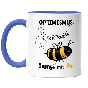 Può includere: Tazza in ceramica bianca con bordo e manico blu. La tazza presenta un'ape di cartone animato nera e gialla con il testo "OPTIMISMUS heisst rückwärts Sumsi mit Po" in nero.