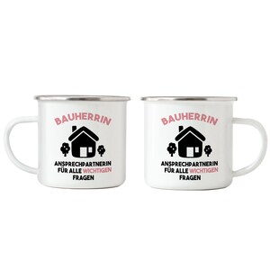 May include: Two white enamel mugs with black and pink text and a black house icon. The text reads "Bauherrin Ansprechpartnerin f&uuml;r alle wichtigen Fragen".
