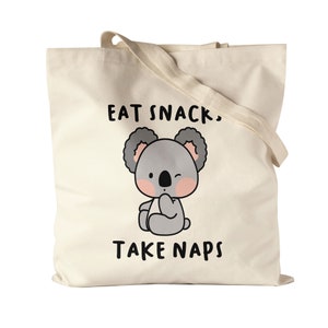 Könnte beinhalten: Eine beige Tragetasche mit einem Karikatur-Koala und dem Text "Eat Snacks, Take Naps".