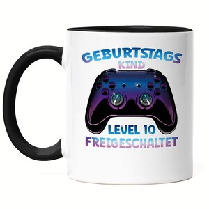 Könnte beinhalten: Weiße Keramiktasse mit schwarzem Henkel und schwarzem Rand. Die Tasse hat eine Grafik eines lila und blauen Videospielcontrollers mit dem Text "Geburtstagskind Level 10 Freigeschaltet" darauf gedruckt.
