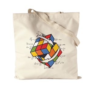 Puede incluir: Una bolsa de tela blanca con un diseño de cubo de Rubik colorido y ecuaciones matemáticas impresas en ella. Las ecuaciones incluyen: √5, π=3.14, 2=√2, 2x2-1=x, Fd=Fode, wow, 6)=RT, AIt, EP.
