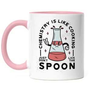 Könnte beinhalten: Weiße Keramiktasse mit rosafarbenem Rand und Henkel. Die Tasse zeigt eine Comic-Illustration eines Bechers mit einem Gesicht und dem Text "Chemie ist wie Kochen - Lecke einfach nicht den Löffel."