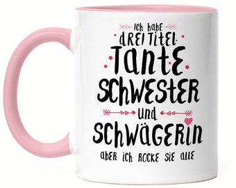 May include: White ceramic mug with a pink rim and handle. The mug has black text that reads "Ich habe drei Titel: Tante, Schwester und Schwägerin, aber ich rocke sie alle".