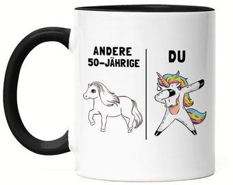 Op de afbeelding: Witte keramische mok met een zwarte handgreep en binnenkant. De mok heeft een humoristisch ontwerp met een pony en een dabende eenhoorn, met de Duitse tekst "ANDERE 50-JÄHRIGE" en "DU".