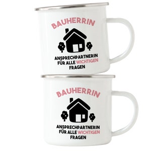 May include: Two white enamel mugs with black and pink text and a black house icon. The text on the mugs reads "Bauherrin Ansprechpartnerin f&uuml;r alle wichtigen Fragen".