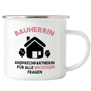 May include: White enamel mug with a black house and trees graphic. The text "Bauherrin Ansprechpartnerin f&uuml;r alle wichtigen Fragen" is printed in pink.