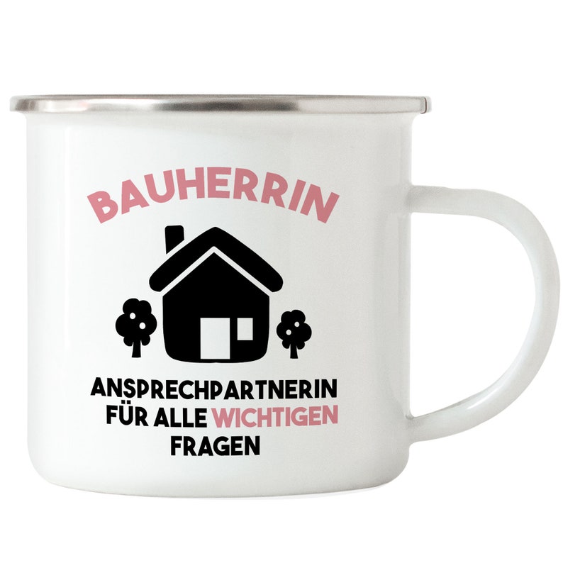 May include: White enamel mug with a black house and trees graphic. The text "Bauherrin Ansprechpartnerin f&uuml;r alle wichtigen Fragen" is printed in pink.