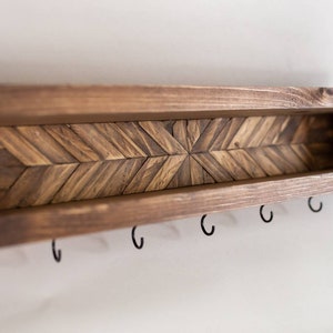 May include: A wooden shelf with a chevron pattern and five hooks. The shelf is stained a dark brown color.