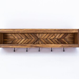 May include: A wooden key holder with a chevron pattern and five hooks. The key holder is stained a dark brown color.