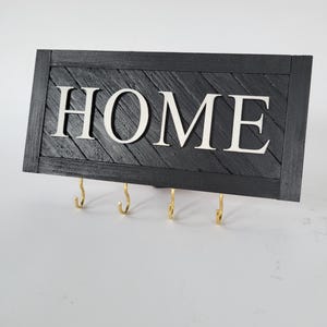 May include: Black wooden key holder with the word "HOME" in white letters and five gold hooks.
