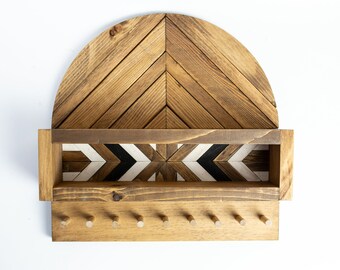 May include: Wooden wall-mounted key holder and shelf. The shelf has a semi-circular top with a chevron pattern. Below is a rectangular shelf with a geometric design in black, white, and brown. The key holder has six pegs.