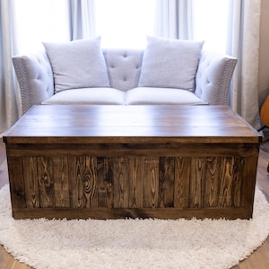 May include: A dark brown wooden coffee table with a rectangular top and a storage compartment. The table is sitting on a white fluffy rug in a living room.