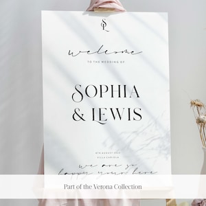 May include: A white wedding welcome sign with black text that reads "Welcome to the wedding of Sophia & Lewis". The date "8th August 2023" and the location "Villa Cariola" are also included. The sign has a handwritten message that says "We are so happy you're here." and the text "Part of the Verona Collection".