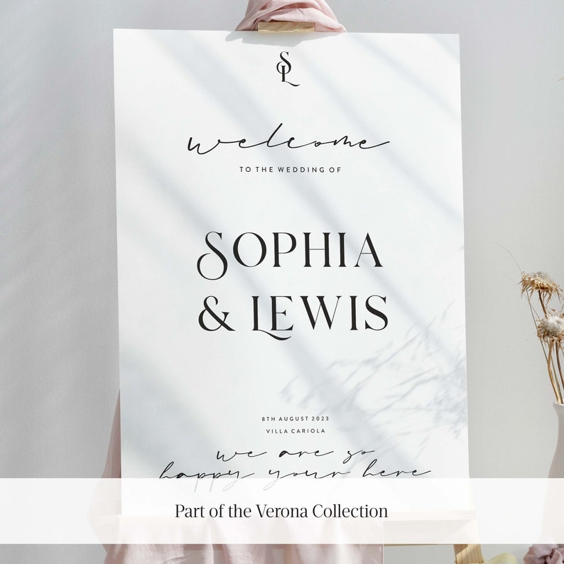 May include: A white wedding welcome sign with black text that reads "Welcome to the wedding of Sophia & Lewis". The date "8th August 2023" and the location "Villa Cariola" are also included. The sign has a handwritten message that says "We are so happy you're here." and the text "Part of the Verona Collection".