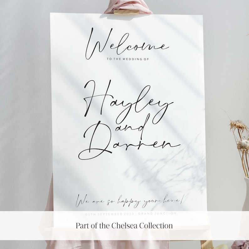 May include: A white welcome sign with black calligraphy text that reads "Welcome to the wedding of Hayley and Darren." The sign also includes the date "05th September 2023" and the location "Grand Junction". The sign is part of the Chelsea Collection.