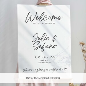 May include: White wedding welcome sign with black calligraphy text that reads "Welcome to the wedding of Julia & Sefano 03.08.23 Gran Mirci 98164 Messina Italy We are so glad you could make it! Part of the Messina Collection"
