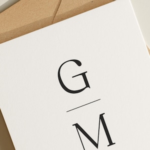 May include: A white card with a black monogram of the letters "G" and "M" with a line separating the letters.