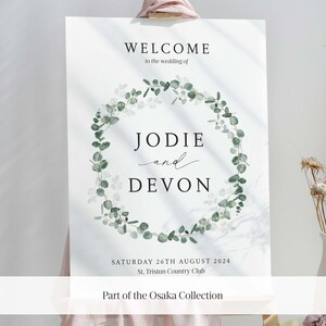 May include: A wedding welcome sign with a green eucalyptus wreath and the text "WELCOME to the wedding of JODIE and DEVON SATURDAY 26TH AUGUST 2024 St. Tristan Country Club Part of the Osaka Collection"