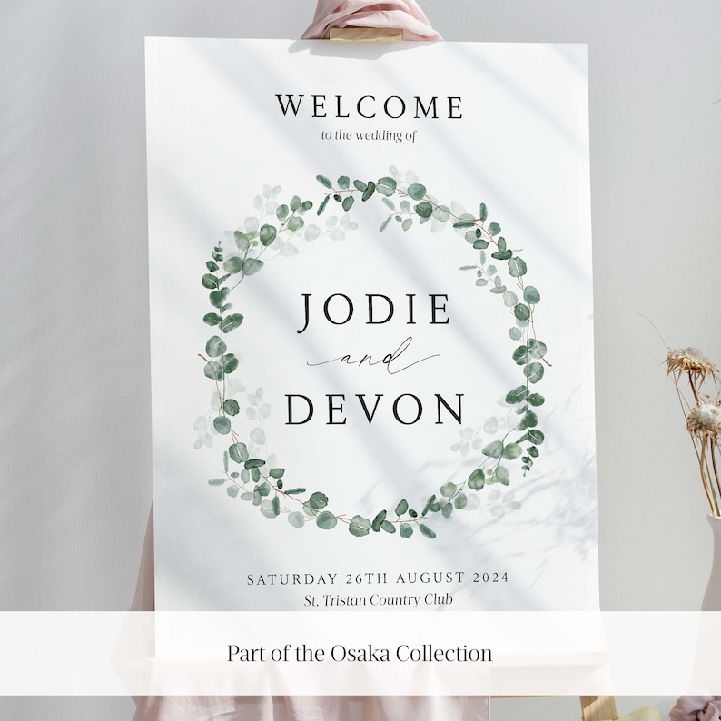 May include: A wedding welcome sign with a green eucalyptus wreath and the text "WELCOME to the wedding of JODIE and DEVON SATURDAY 26TH AUGUST 2024 St. Tristan Country Club Part of the Osaka Collection"