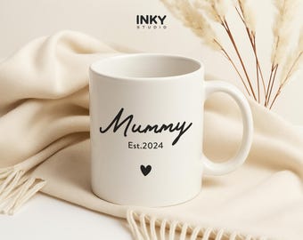 Puede incluir: Taza de cerámica blanca con texto negro que dice "Mummy Est. 2024" y un pequeño corazón negro.
