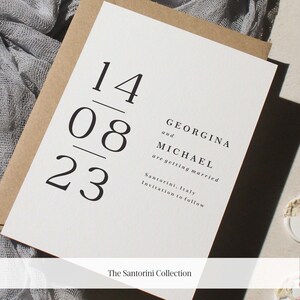 K&ouml;nnte beinhalten: Eine wei&szlig;e Hochzeitseinladungskarte mit schwarzem Text. Das Datum ist der 14.08.23. Der Text lautet "Georgina und Michael heiraten. Santorini, Italien. Einladung folgt."