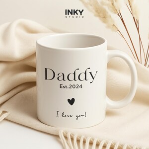 Puede incluir: Taza de cerámica blanca con texto negro que dice "Daddy Est. 2024 I love you!" con un pequeño corazón negro.