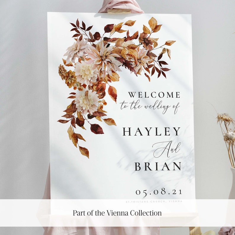 May include: A wedding welcome sign with a watercolor floral design in shades of brown, orange, and cream. The sign reads "Welcome to the wedding of Hayley and Brian 05.08.21 St. Tristans Church, Vienna. Part of the Vienna Collection."