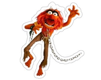 May include: A cartoon illustration of a red and orange Muppet character with a chain around its neck. The character is wearing brown pants and has a wild red mane of hair. The character is in a dynamic pose with its arms and legs outstretched.