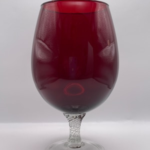 May include: A large, deep red glass goblet with a clear, twisted stem and base. The goblet is ideal for serving cocktails or wine.