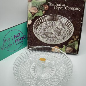May include: A clear, three-sectioned Durham Crystal Company relish dish with a diamond pattern. The dish is round with a scalloped edge and is displayed with its original box, which features a picture of the dish and vegetables.