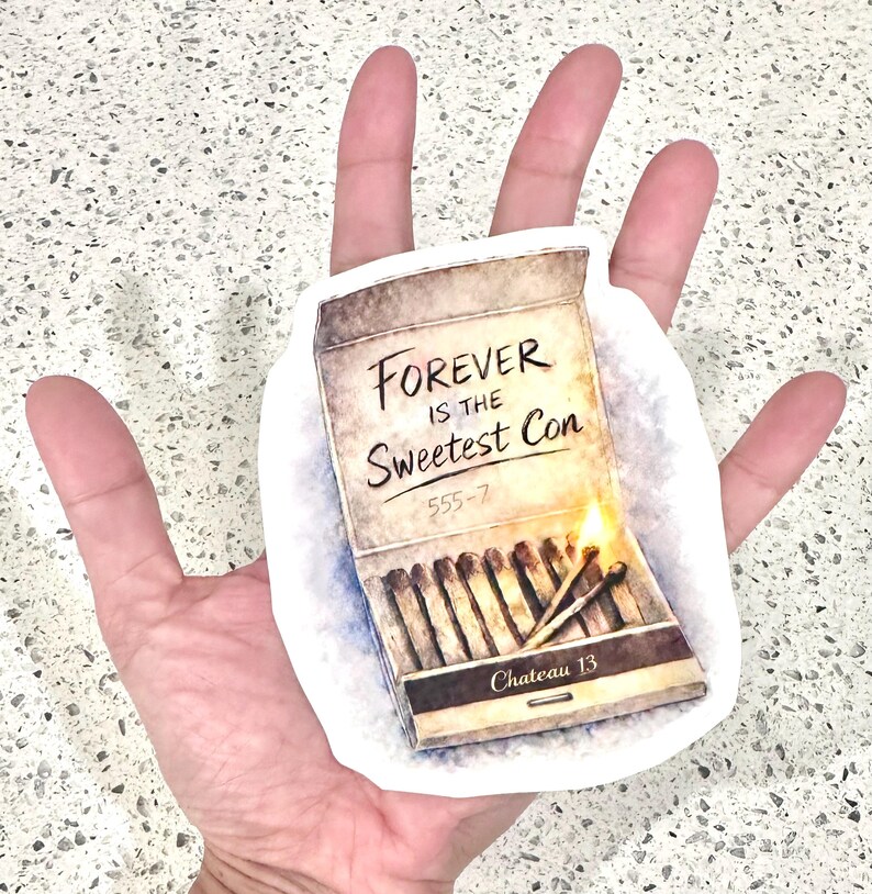 May include: A sticker featuring a matchbox design with the text "Forever is the Sweetest Con." The matchbox is open, with several matches and two lit matches. The sticker has a white border.