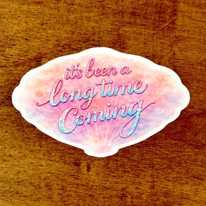 May include: A white ceramic mug with a black handle and the text "But First, Coffee" in a handwritten style. The mug is on a white surface. The mug is likely used for hot beverages.