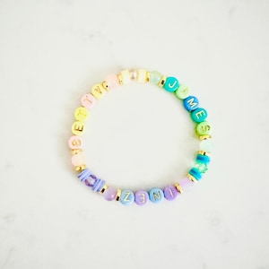 Könnte beinhalten: Ein Regenbogen-Perlenarmband mit dem Namen "Elizabeth James", der in goldenen Buchstaben geschrieben ist.