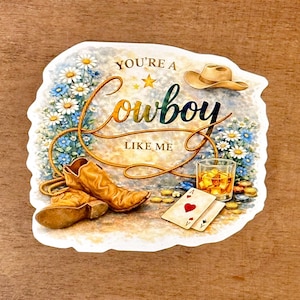 May include: A sticker with a cowboy theme. It features a cowboy hat, boots, a glass of whiskey, playing cards, and the text "You're a Cowboy Like Me" surrounded by flowers and a rope.