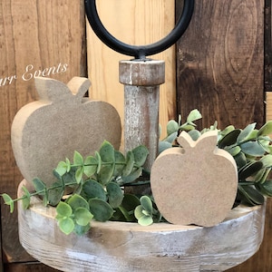 May include: Two unfinished wooden apple shapes on a tiered wooden tray with greenery. The tray is attached to a black metal stand.