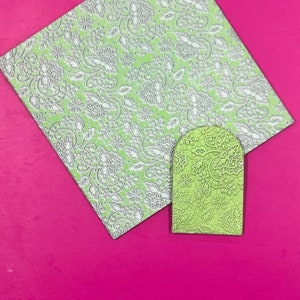 May include: Two green pieces of paper with a white lace pattern. The larger piece is a square and the smaller piece is a rectangle with rounded corners.