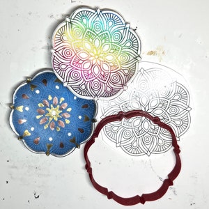 Puede incluir: Tres diseños de mandalas, uno con colores arcoíris, otro con acentos dorados y cobrizos sobre un fondo azul, y uno con un contorno de mandala en blanco. Los diseños están sobre una superficie blanca.