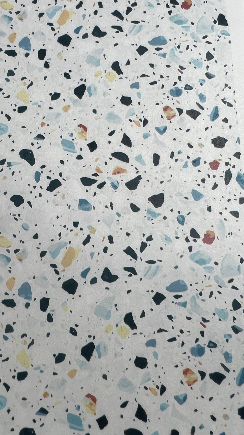 Op de afbeelding: Een close-up van een wit oppervlak met een terrazzo-patroon. Het oppervlak is bedekt met kleine, kleurrijke steentjes, waaronder zwart, blauw, geel en rood.