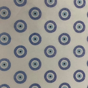 May include: White background with a repeating pattern of blue and white evil eye charms. The charms are drawn in a simple style with a black pupil in the center.