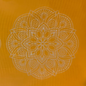 Puede incluir: Un diseño de mandala blanco sobre un fondo amarillo. El mandala es intrincado y detallado, con un patrón circular de flores y hojas.