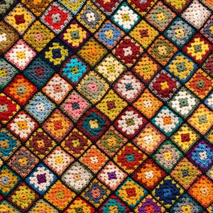 Może przedstawiać: Ręcznie wykonany szydełkowy koc z powtarzającym się wzorem wielokolorowych kwadratów typu granny square ułożonych w romby. Każdy kwadrat składa się z centralnego motywu kwiatowego otoczonego kontrastującymi kolorami włóczki, w tym czerwonym, niebieskim, żółtym, zielonym, pomarańczowym, fioletowym i białym.